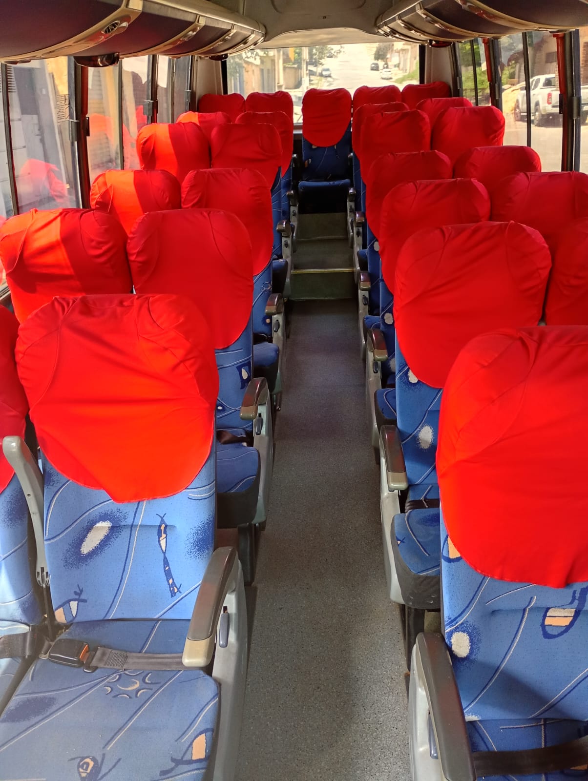 Interior do micro-ônibus com poltronas vermelhas e azuis